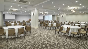 Un amplio salón de conferencias con mesas y sillas redondas, una pantalla de proyector y una alfombra estampada.