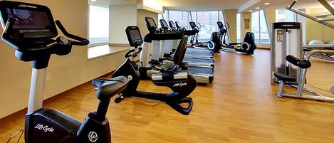 A gym with multiple exercise machines, including treadmills and stationary bikes, arranged in rows.