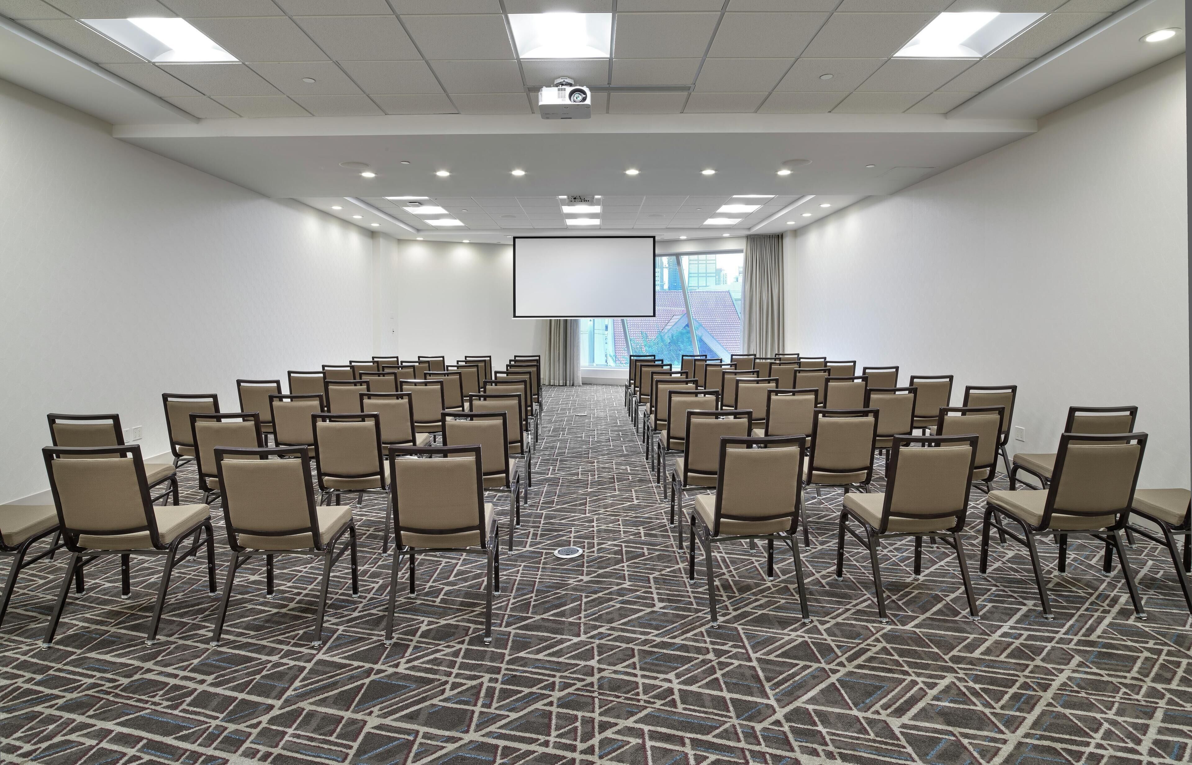 A conference room with rows of chairs, a large screen, and a projector.