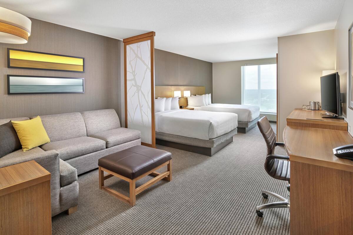 A hotel room with a sofa, two beds, a desk, a chair, and a TV.
