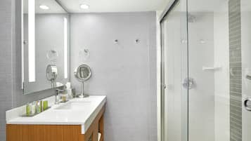 Un baño moderno con tocador de madera, un espejo redondo y mampara de vidrio.
