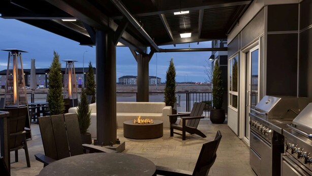 An outdoor patio area with a round table, chairs, a fire pit, and a grill.