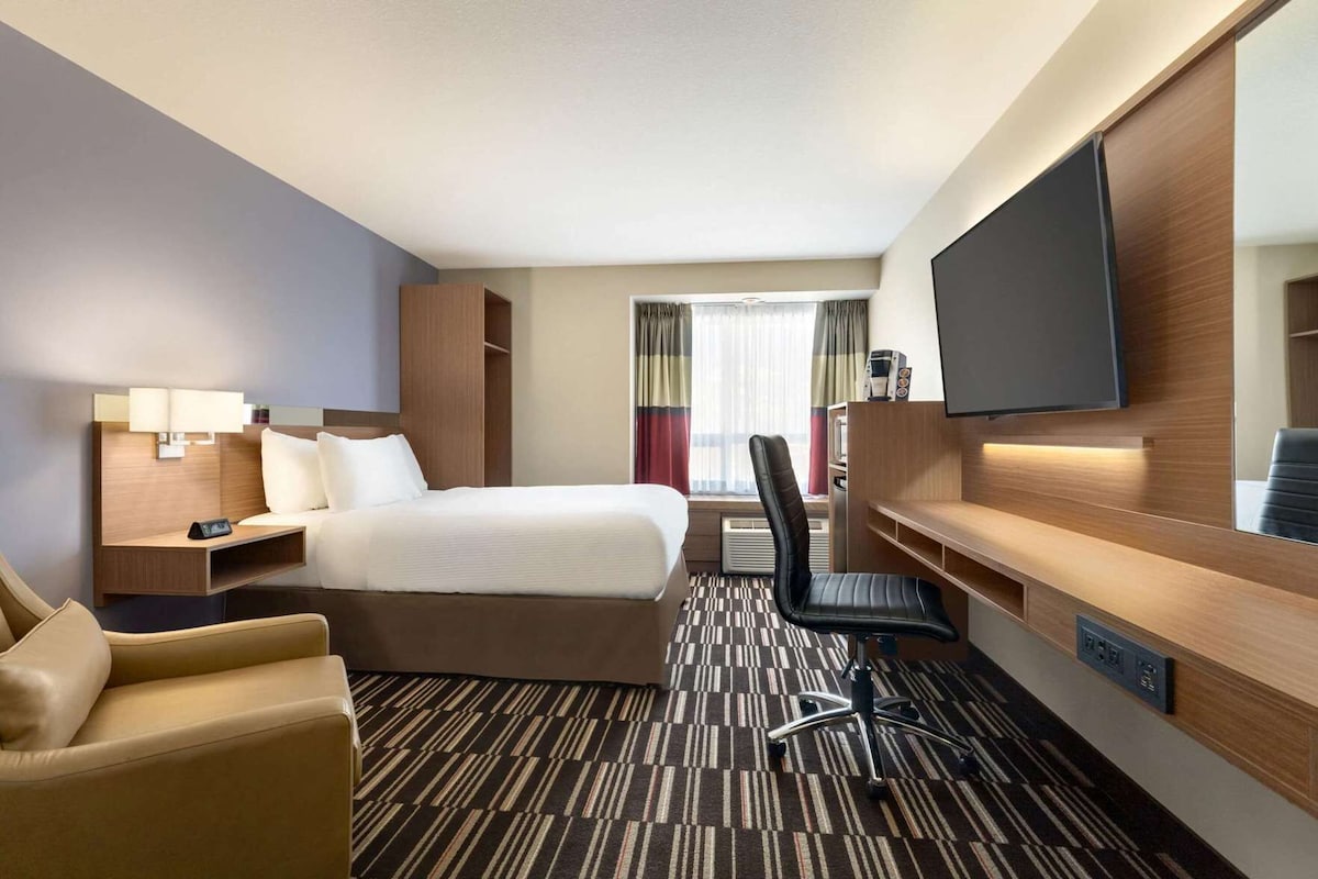 Une chambre d’hôtel avec un lit, un bureau, une chaise, une télévision et une fenêtre avec des rideaux.