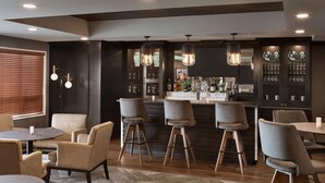 A modern bar area with bar stools, a counter with a variety of bottles, and a seating area with round tables and chairs.