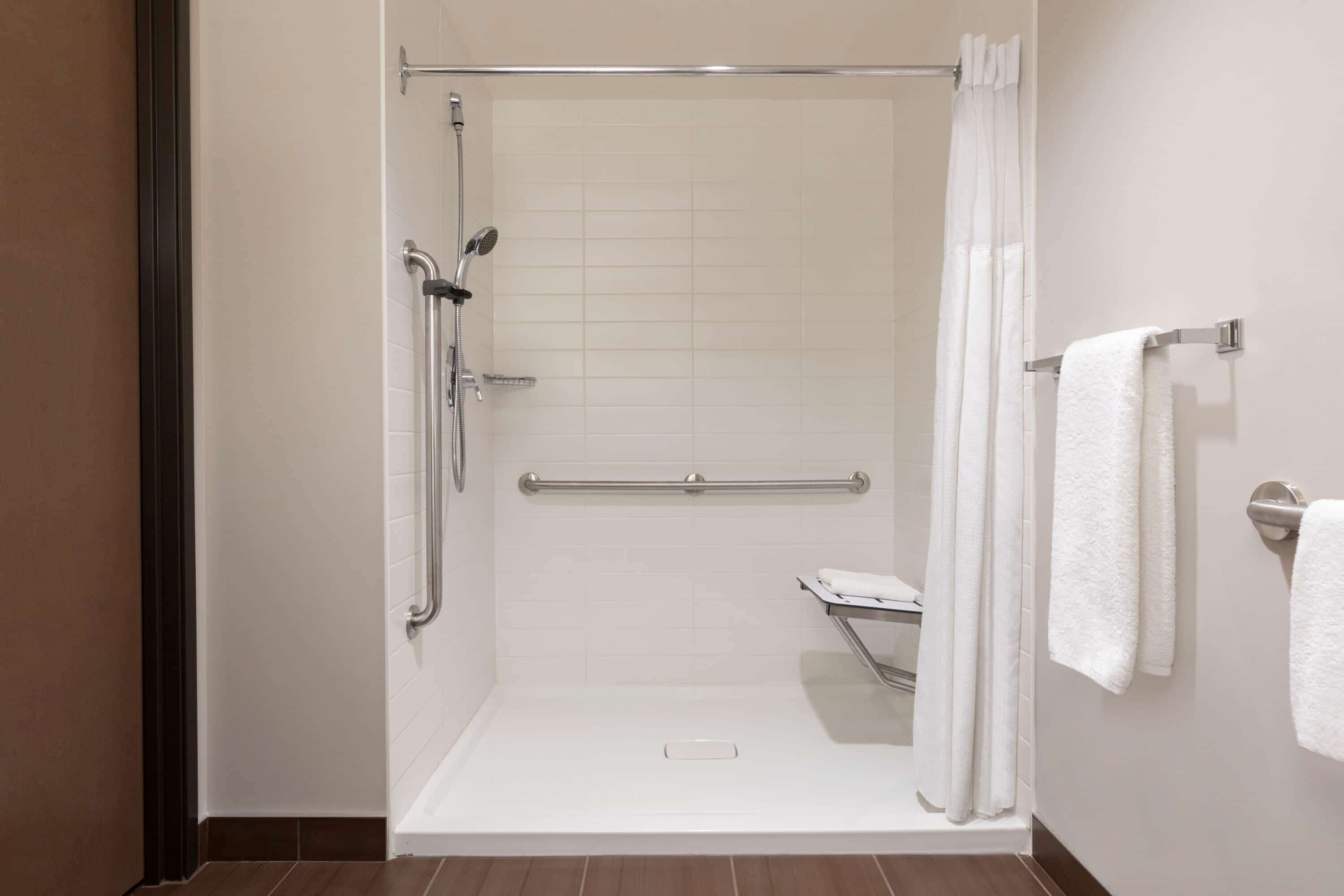 Une douche à l’italienne avec une porte en verre, une barre d’appui et un porte-serviettes avec des serviettes.