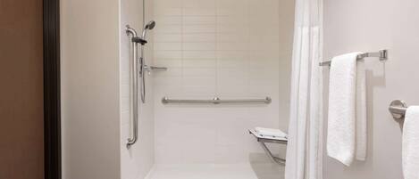 Une douche à l’italienne avec une porte en verre, une barre d’appui et un porte-serviettes avec des serviettes.