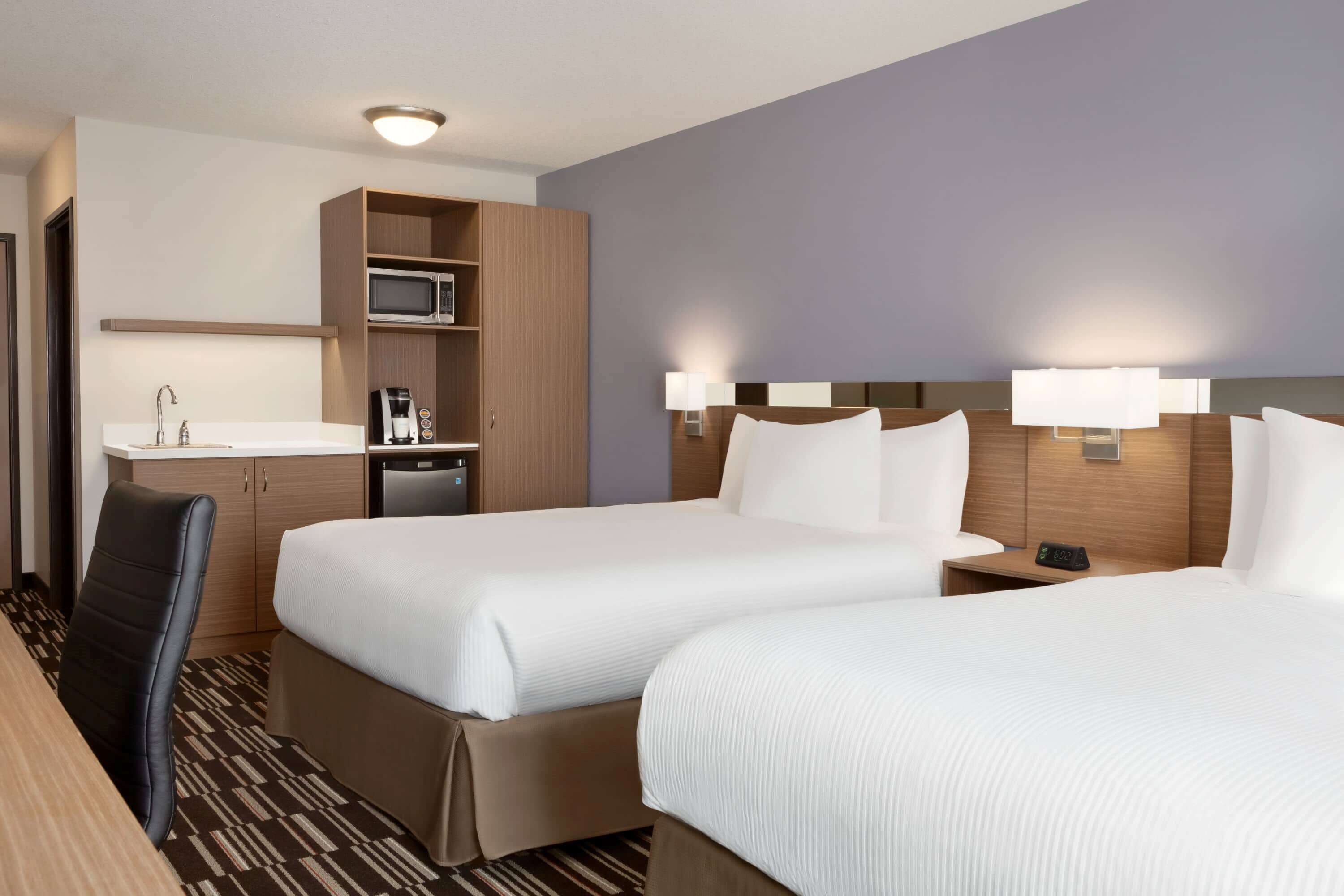 Habitación de hotel con dos camas, un escritorio, un microondas, una cafetera y un lavabo.