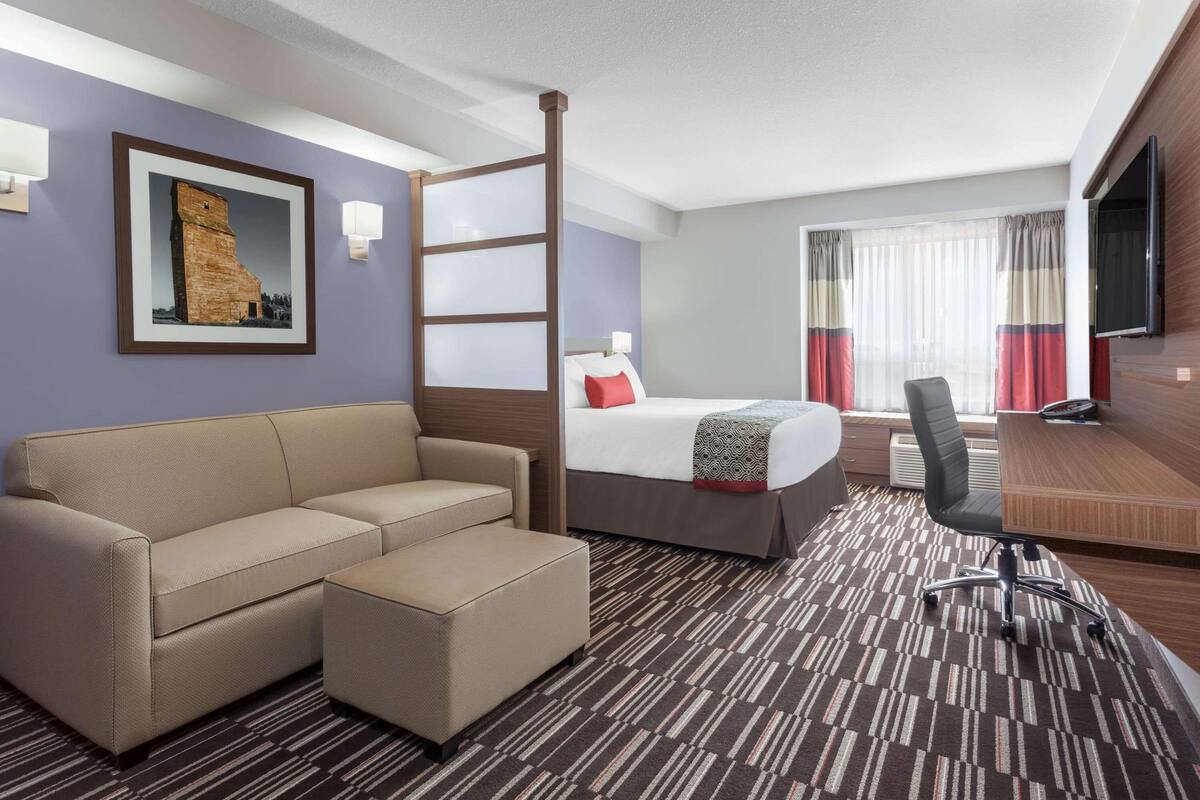 Habitación de hotel con cama, sofá, escritorio, silla, televisión y ventana con cortinas.