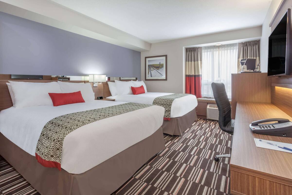 Una habitación de hotel con dos camas, un escritorio con teléfono, una silla y un televisor.
