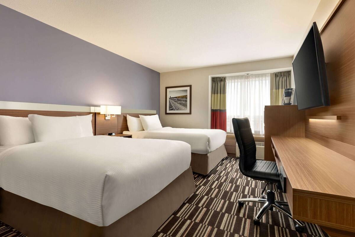 Habitación de hotel con dos camas, un escritorio, una silla, un televisor y una ventana con cortinas.