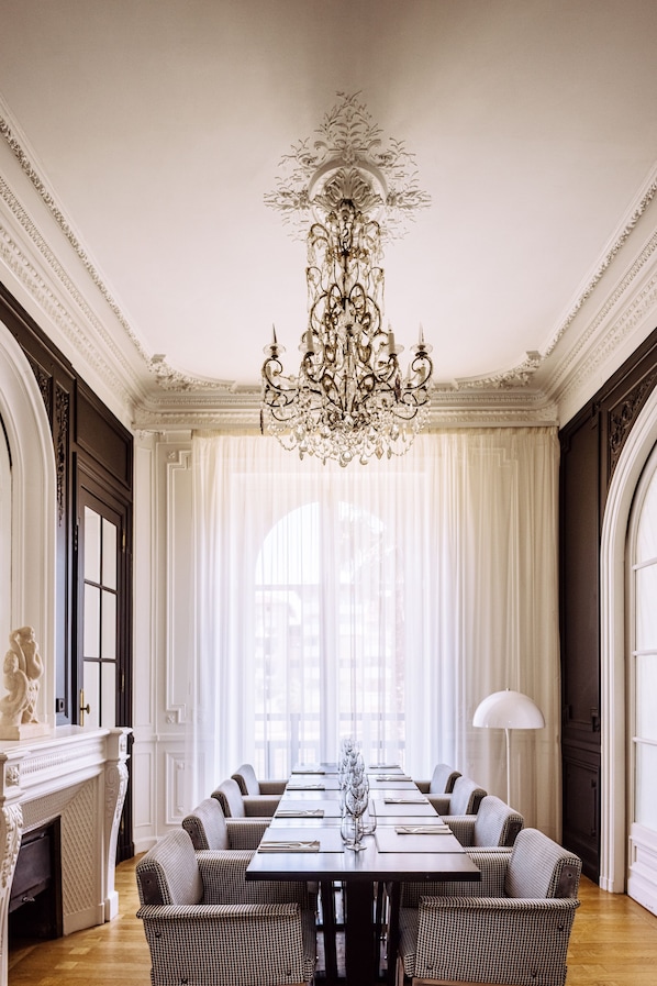 A formal dining room with a long table, upholstered chairs, a chandelier, and a fireplace.