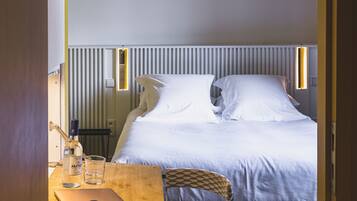 A hotel room with a bed, a desk with a laptop, a chair, a bottle, and a glass.