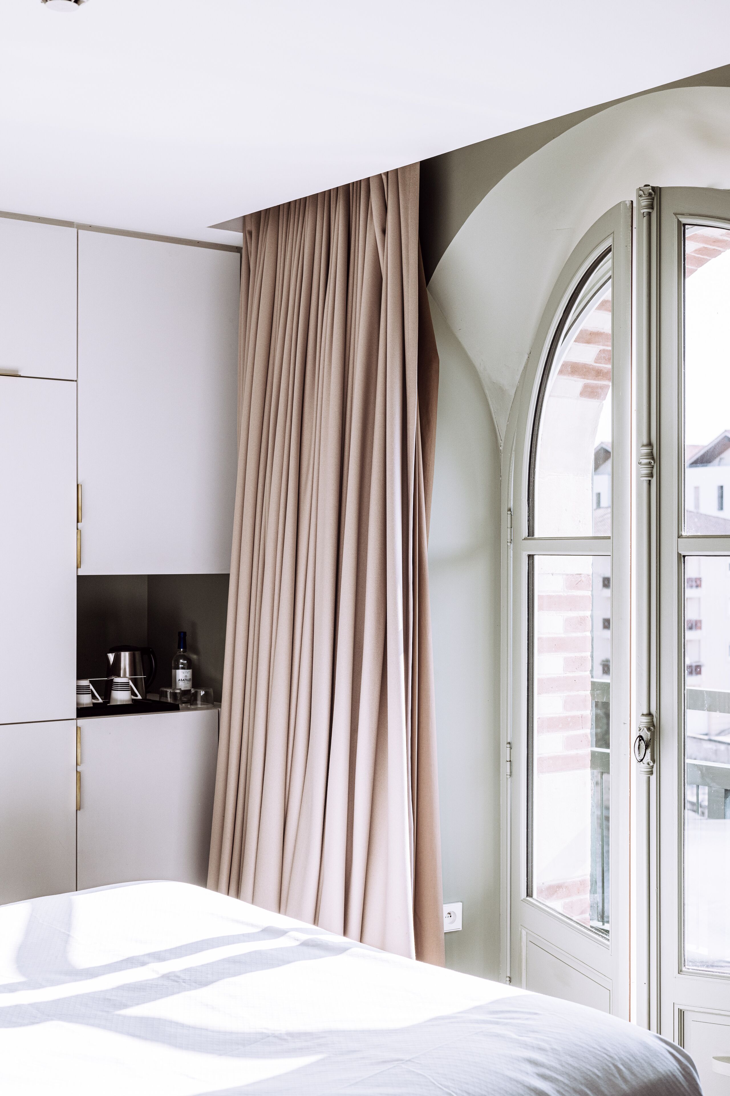 Ein Schlafzimmer mit Bett, einem Vorhangfenster, einer Küchenzeile mit Geräten und Blick auf Gebäude.