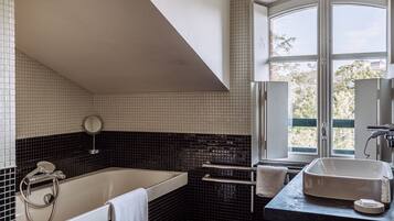 Un bagno moderno con una vasca, un mobile toilette con specchio e una finestra vista alberi.