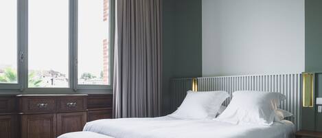A neatly made bed with white linens, a wooden bench, and a nightstand with a lamp.