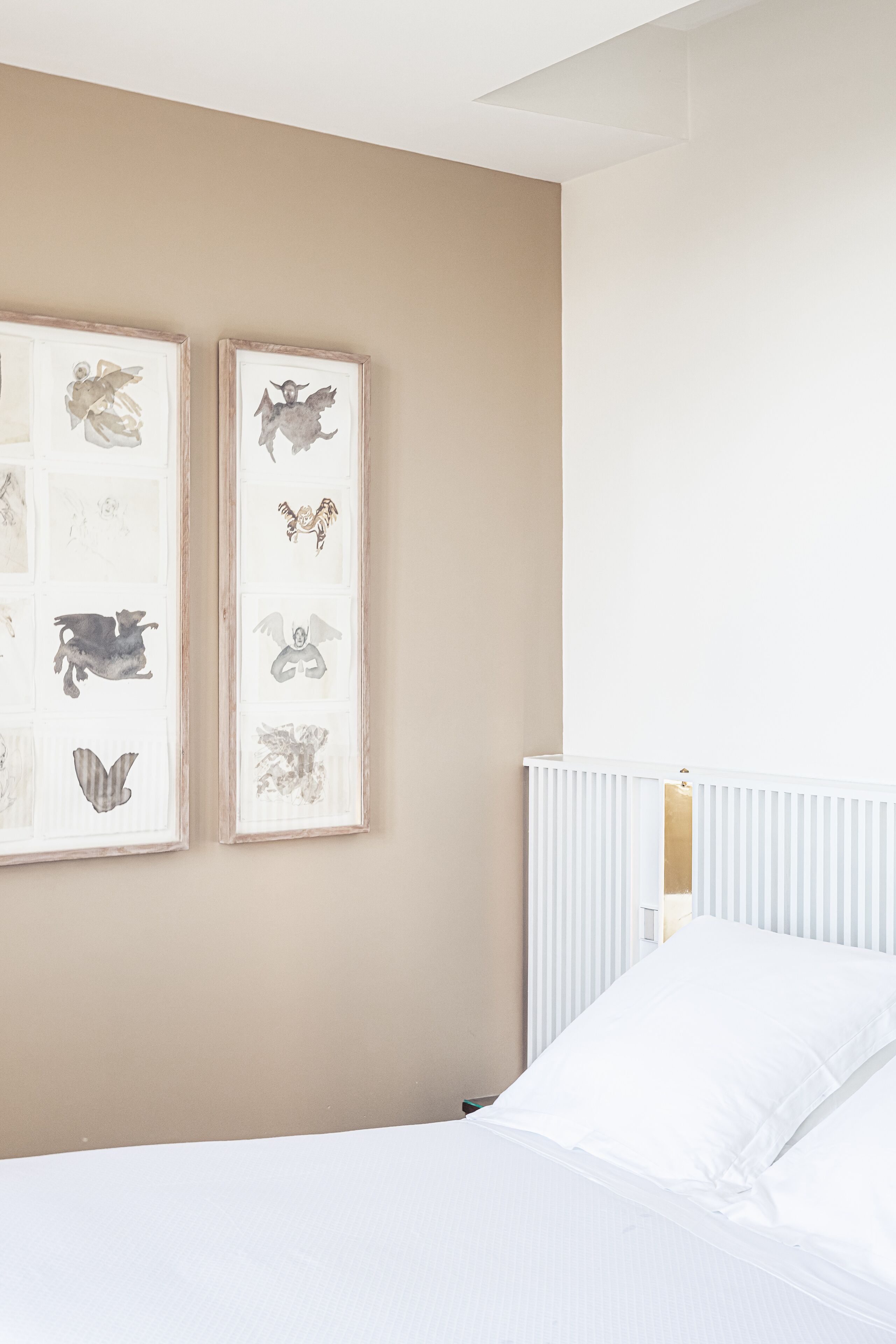 Un dormitorio con una cama, ropa de cama blanca, un radiador y dos cuadros en la pared.