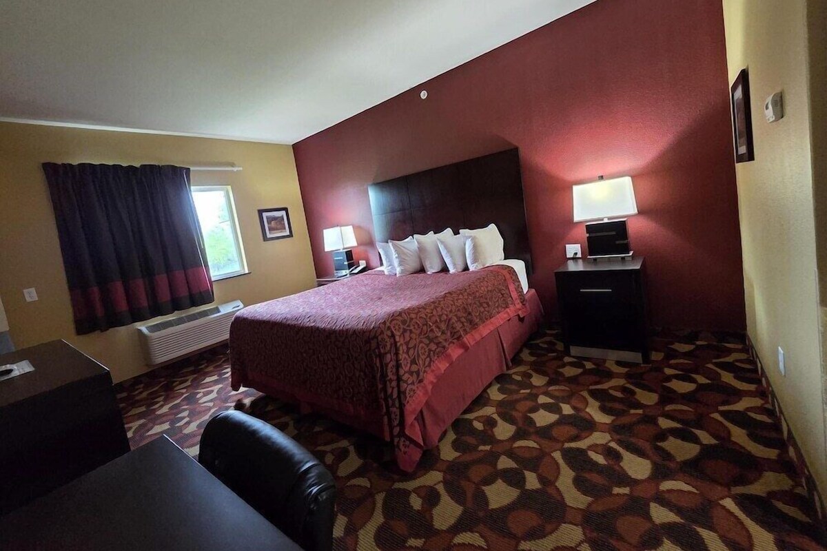 A hotel room with a bed, a desk, a chair, a lamp, and a window with curtains.
