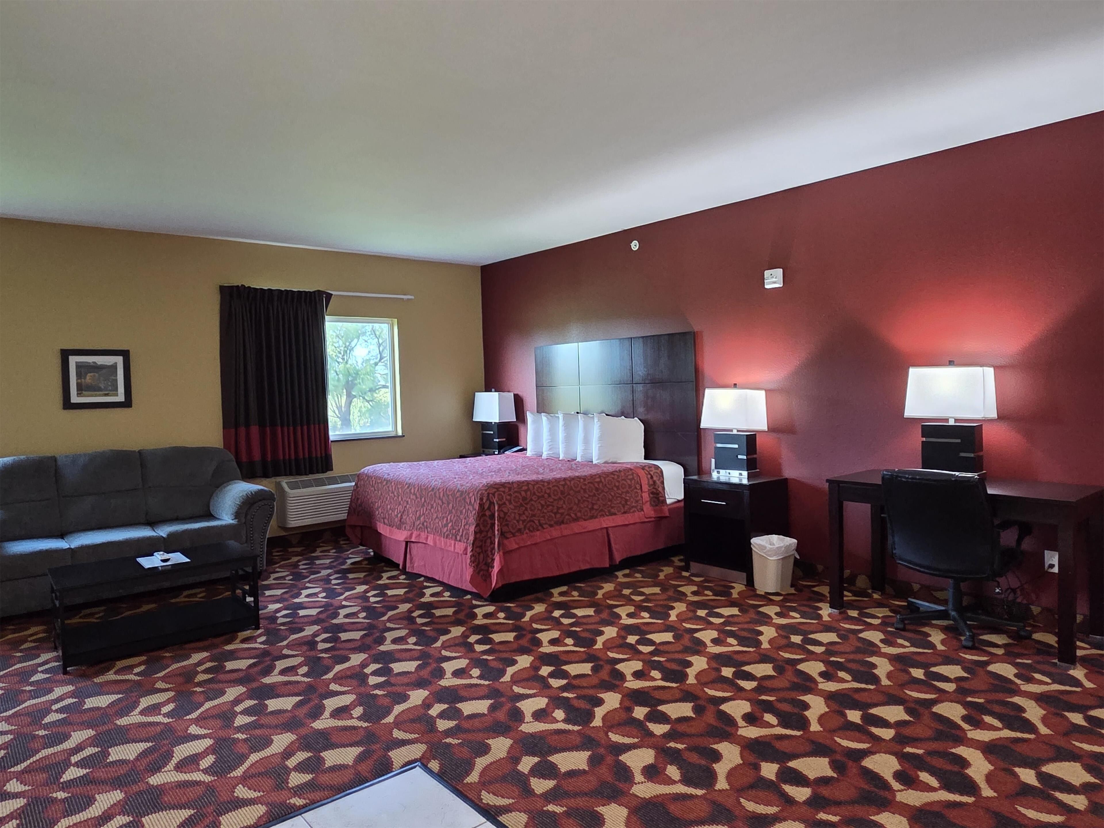 A hotel room with a bed, a desk, a chair, a sofa, and a patterned carpet.
