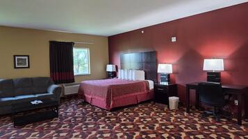 A hotel room with a bed, a desk, a chair, a sofa, and a patterned carpet.