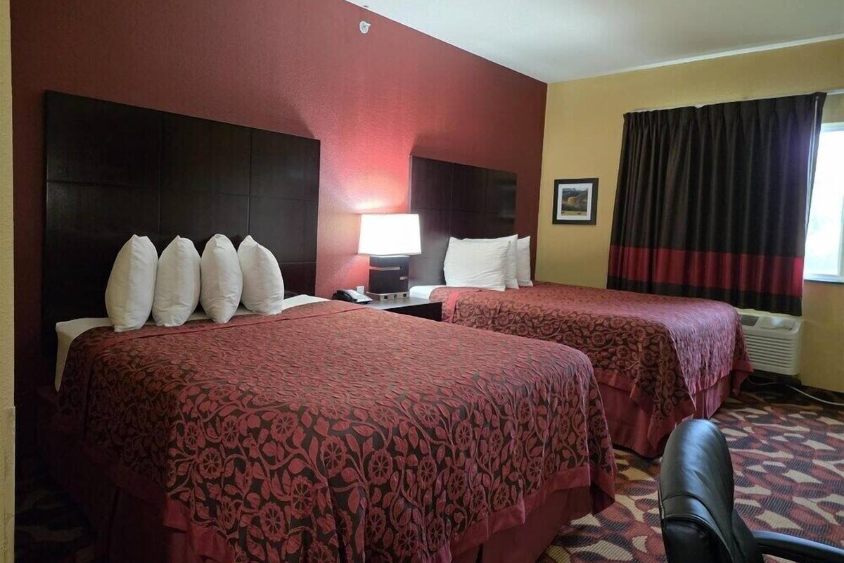 A hotel room with two beds, a desk, a chair, a lamp, and a window with curtains.