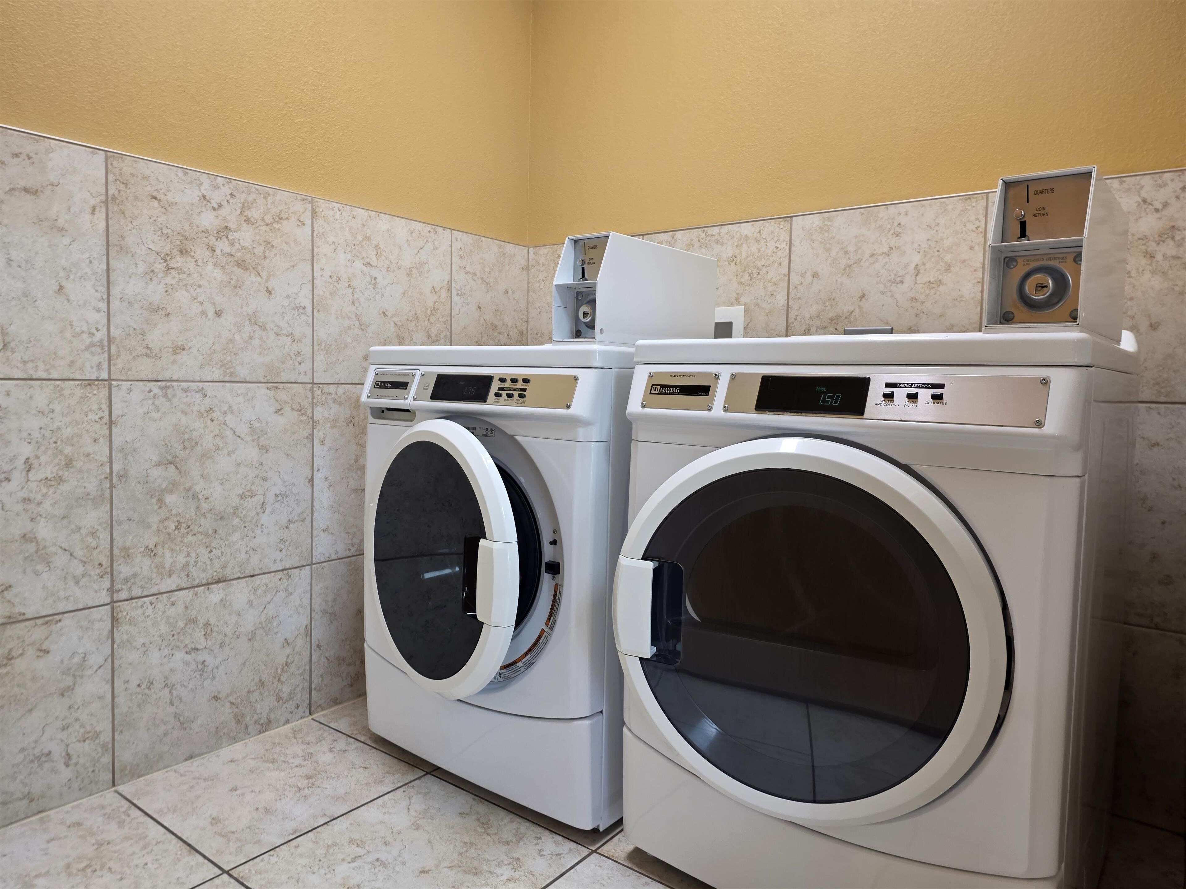 Two front-loading washing machines in a laundry room with tiled walls and floor.