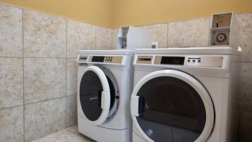 Two front-loading washing machines in a laundry room with tiled walls and floor.