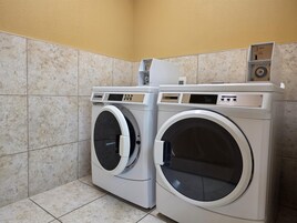 Two front-loading washing machines in a laundry room with tiled walls and floor.