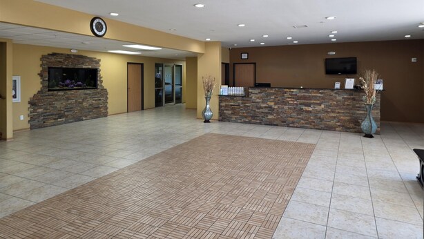 A hotel lobby with a reception desk, a stone fireplace, a clock, and a flat-screen TV on the wall. - SureStay Studio By Best Western El Dorado (El Dorado)