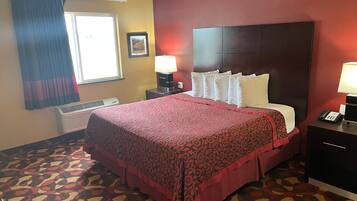 A hotel room with a large bed, a bedside table with a lamp, a window with curtains, and a wall-mounted air conditioner.