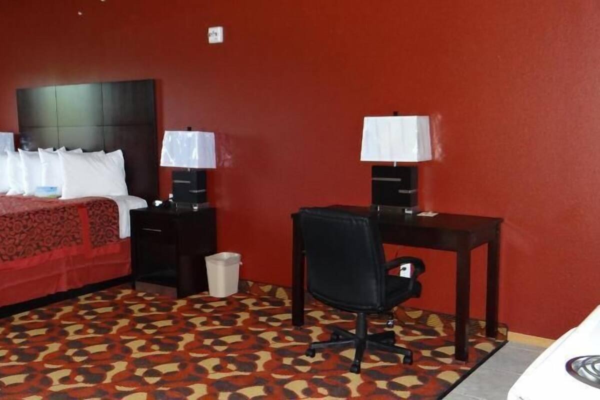 A hotel room with a bed, desk, chair, and a trash bin.