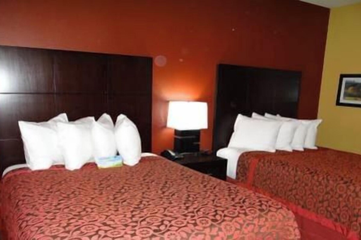 A hotel room with two beds, a nightstand, a lamp, and a framed picture on the wall.