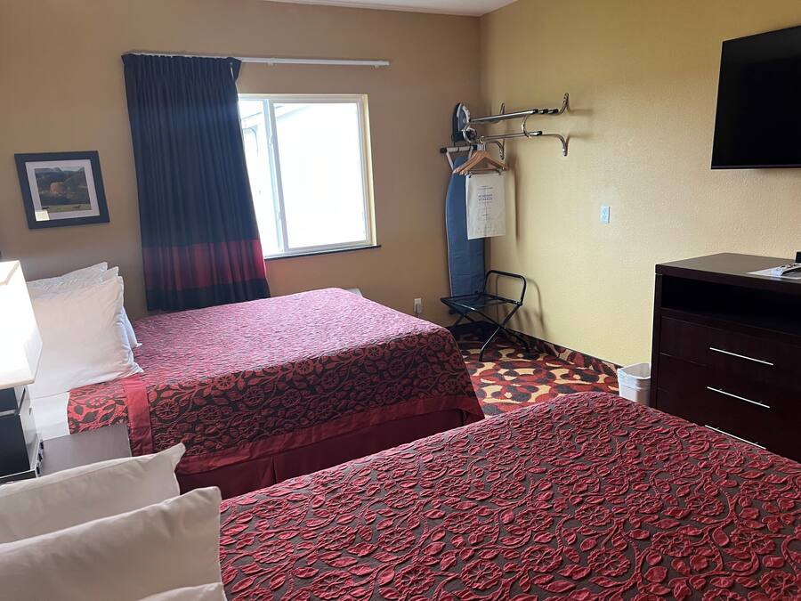 A hotel room with two beds, a desk, a chair, a TV, and a window with curtains.