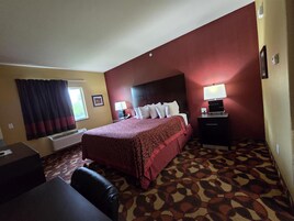 A hotel room with a large bed, a desk, a chair, a TV, and a lamp.