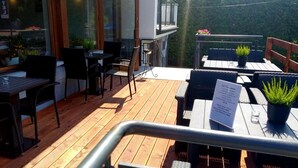 An outdoor patio area with wooden flooring, black wicker furniture, and potted plants. - Hotel Solny (Wieliczka)