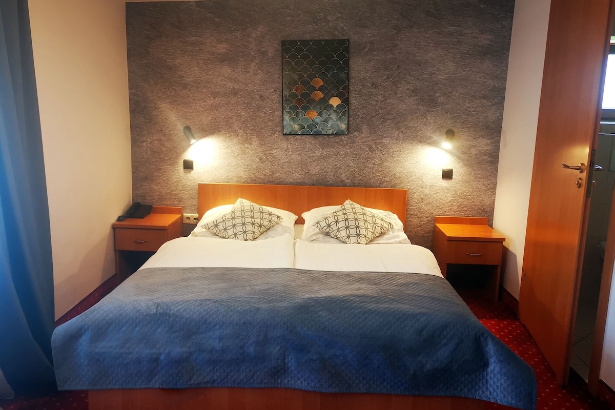 A neatly made bed with a blue blanket, two bedside tables with lamps, a wall-mounted artwork, and a wooden headboard.