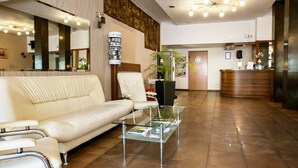 A modern hotel lobby with a reception desk, a white leather sofa, a glass coffee table, and a large mirror. - Hotel Solny (Wieliczka)