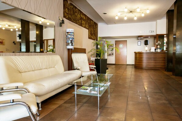 A modern hotel lobby with a reception desk, a white leather sofa, a glass coffee table, and a large mirror. - Hotel Solny (Wieliczka)