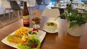 A dining table with a meal consisting of a breaded fish fillet, fries, a salad, and a dessert. A bottle of beer is also visible. - Hotel Solny (Wieliczka)