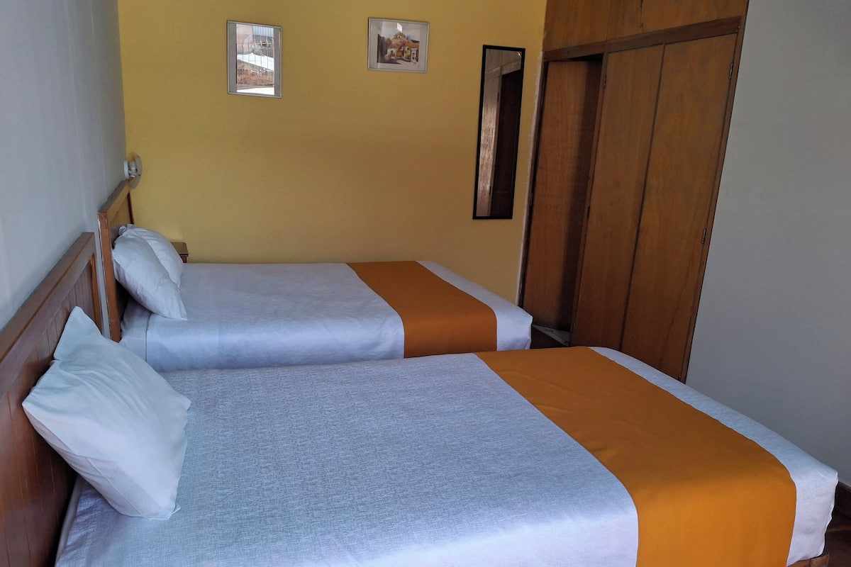 Habitació amb dos llits, amb capçaleres i armari de fusta.