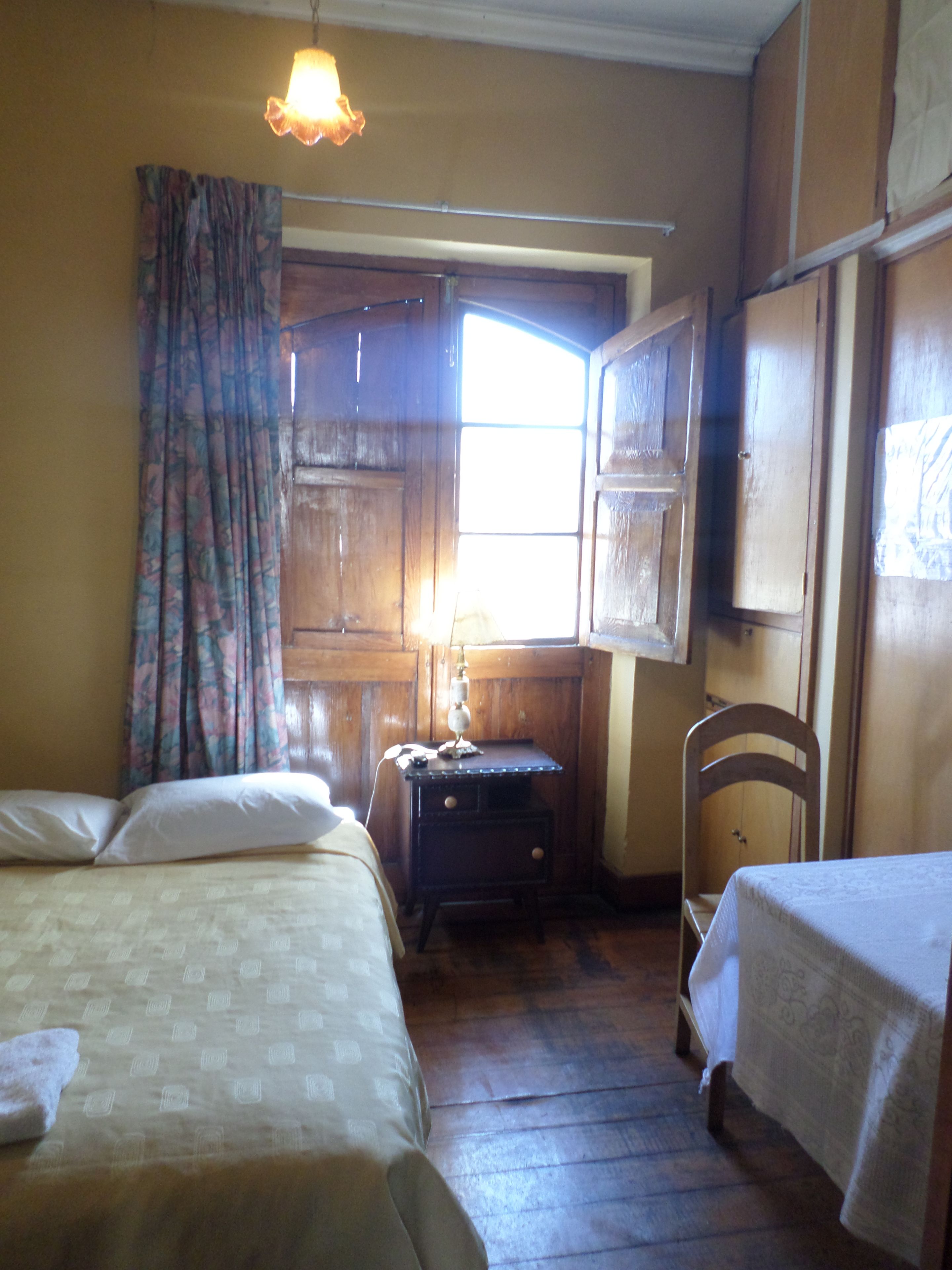 A room with two beds, a wooden dresser, a chair, and a window with curtains.