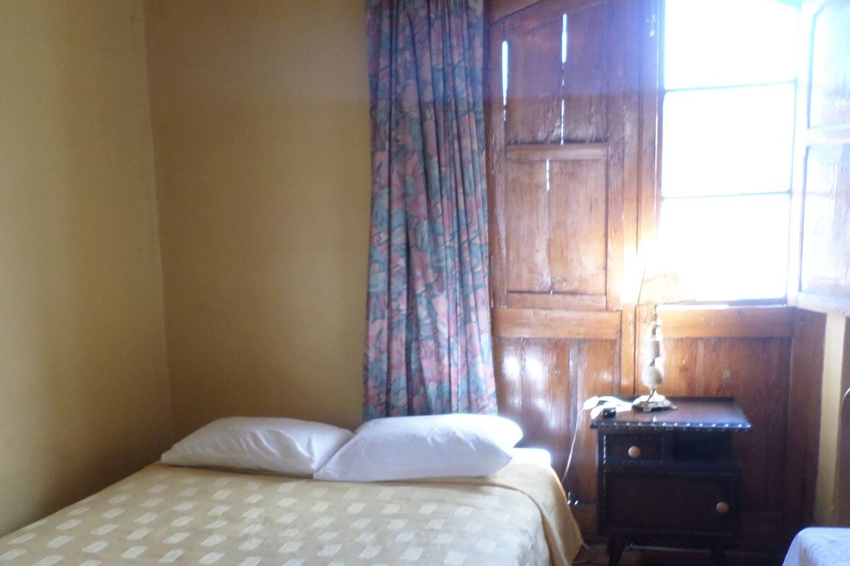 Habitació amb dos llits, un escriptori de fusta i una finestra amb cortines.
