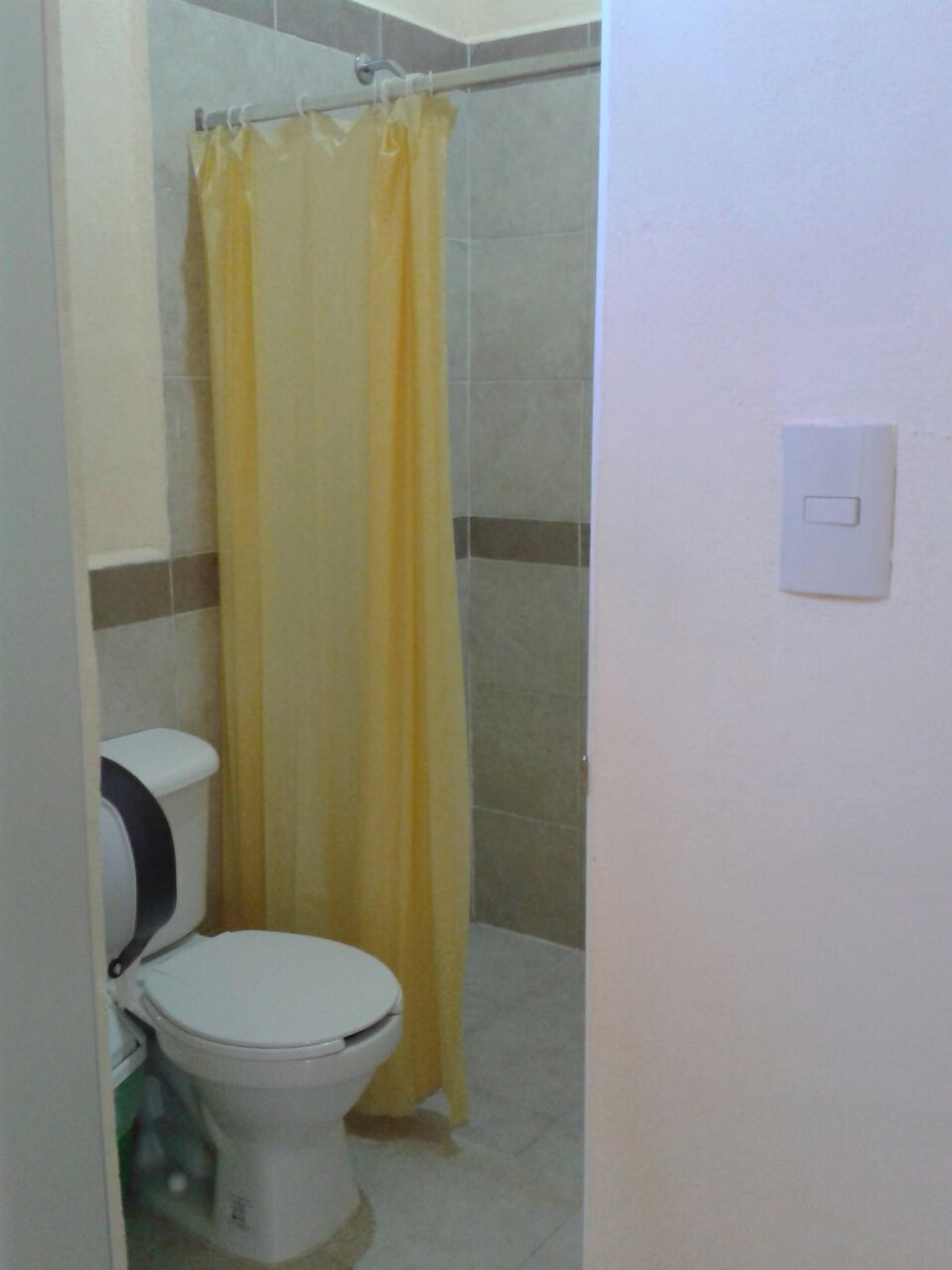 Un baño con inodoro, ducha con cortina amarilla y un interruptor de luz en la pared.