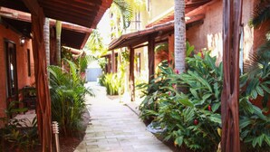 A covered walkway with a brick path, surrounded by lush greenery and palm trees. - Pousada Corais do Sul (Tibau do Sul)