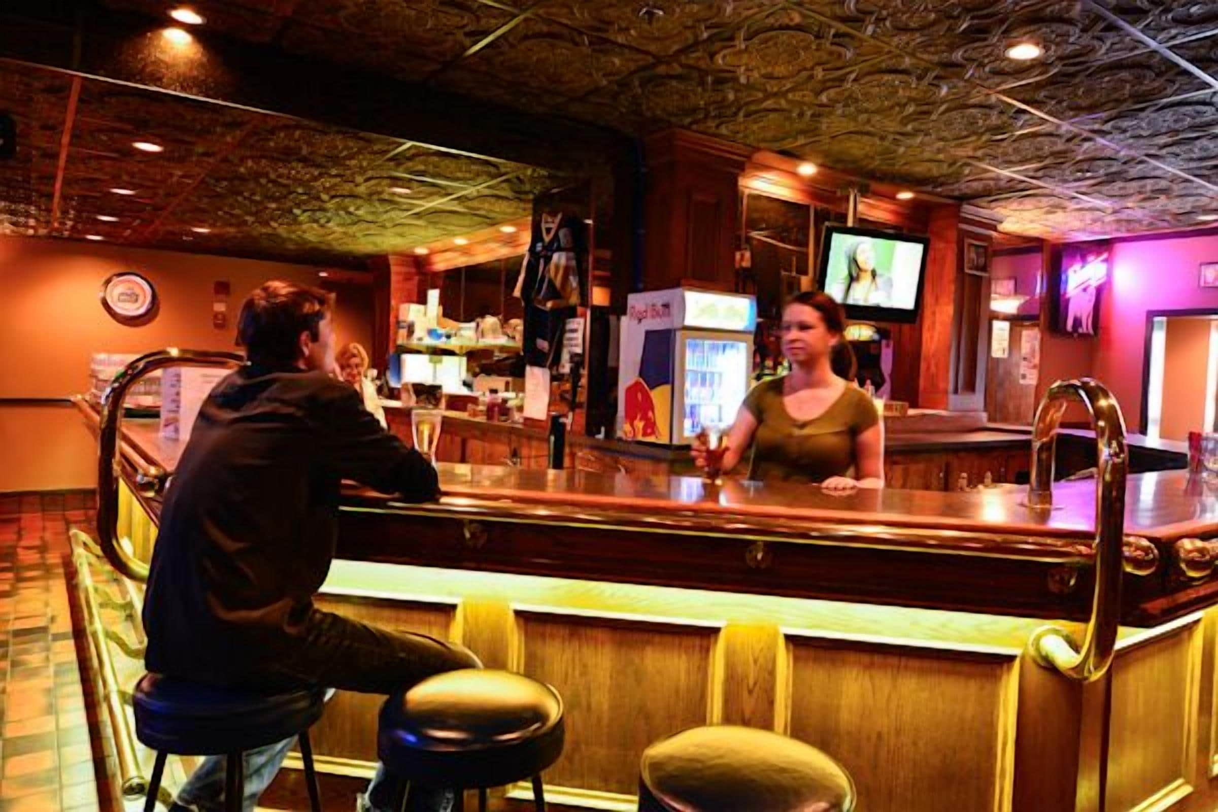 A bar area with a counter, stools, and a television screen.