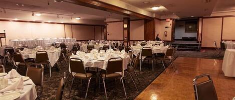 Une salle de banquet avec de nombreuses tables rondes disposées pour le repas, équipées de chaises et de couverts.