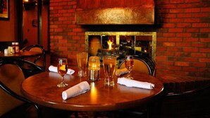 A restaurant interior with a brick wall, a large wood-burning stove, and a table set with glasses and a napkin. - Travelodge by Wyndham Winnipeg Airport West (Winnipeg)