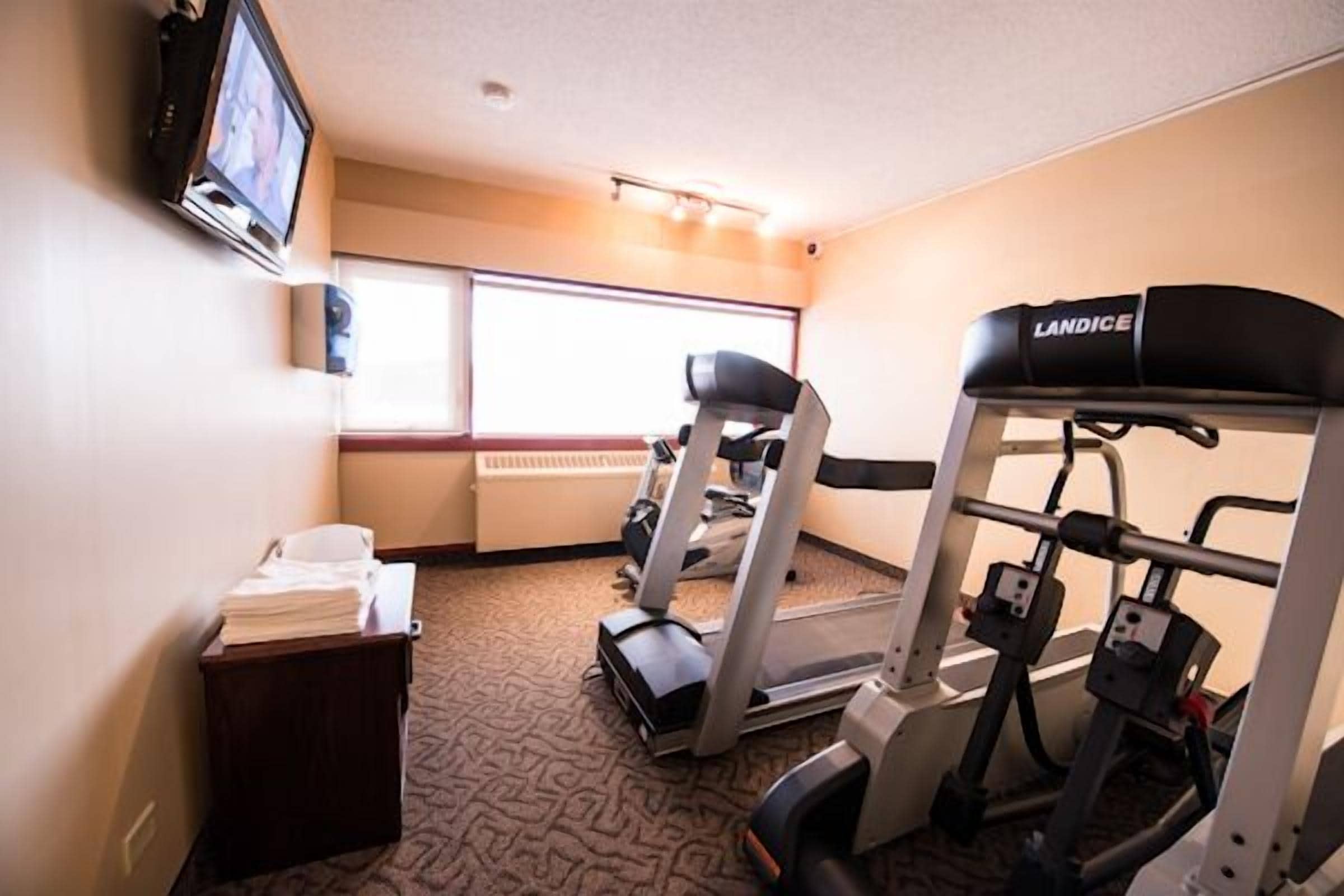 A hotel room with a treadmill, a stationary bike, and a TV mounted on the wall.