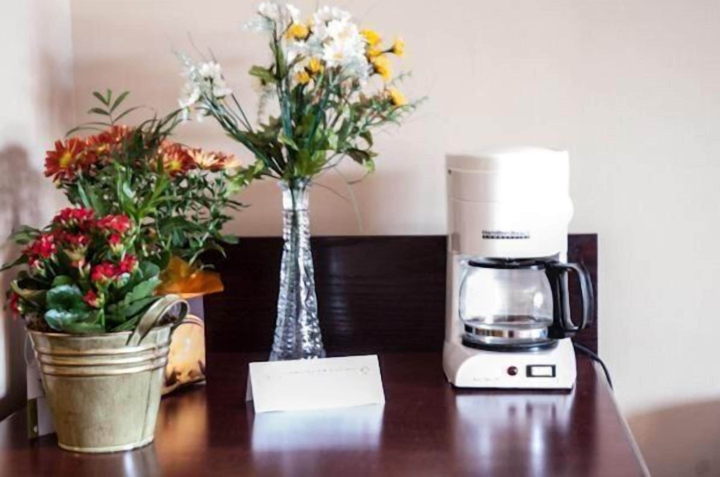 A table with a coffee maker, a vase with flowers, and a metal bucket.