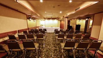 A conference room with rows of chairs, a table with a white tablecloth, and a carpeted floor.