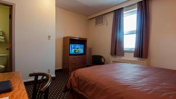 A hotel room with a bed, a TV on a wooden cabinet, a chair, and a window with curtains.
